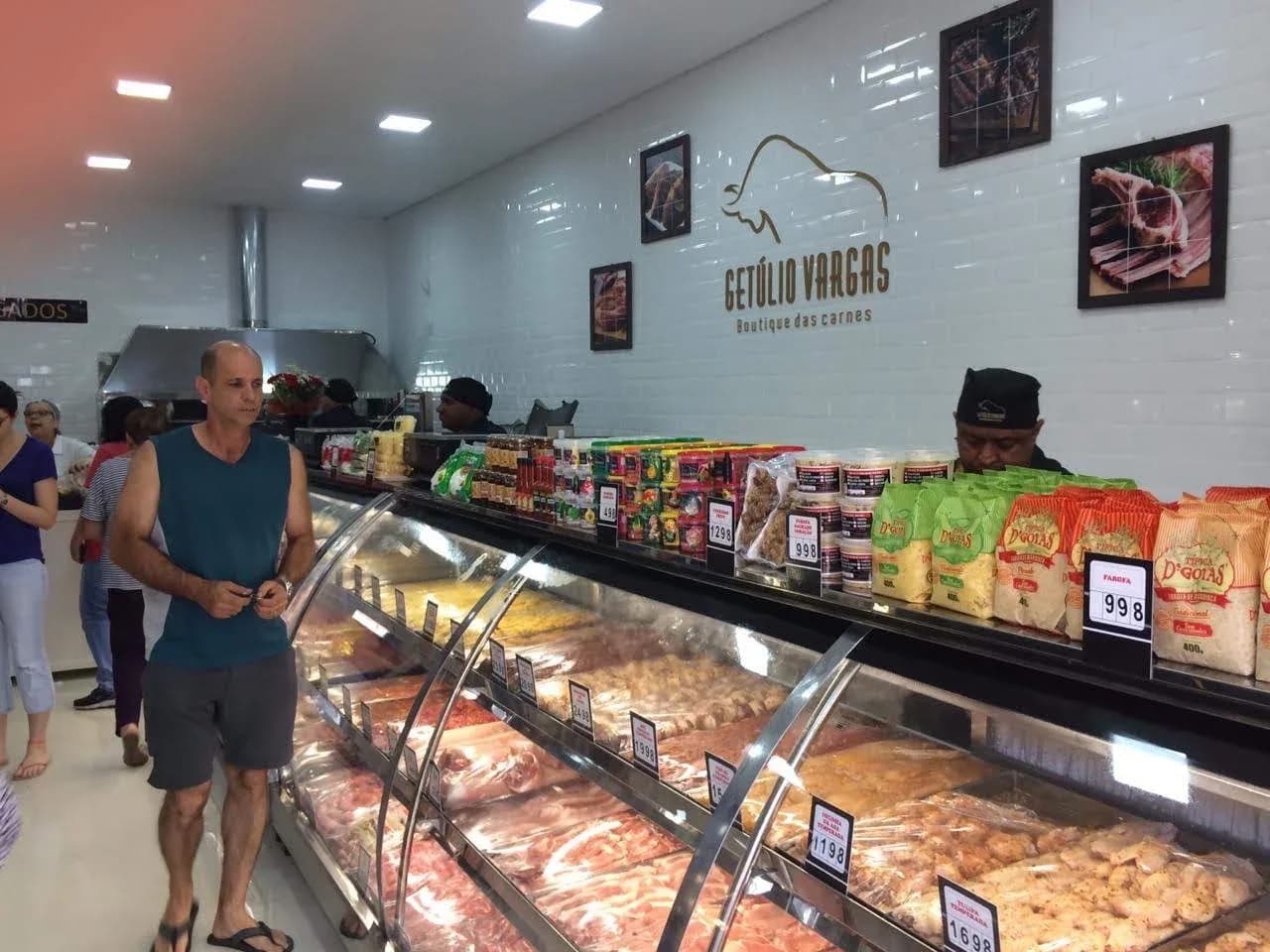 Interior da Getúlio Vargas, com balcão de carnes, pessoas e a marca na parede